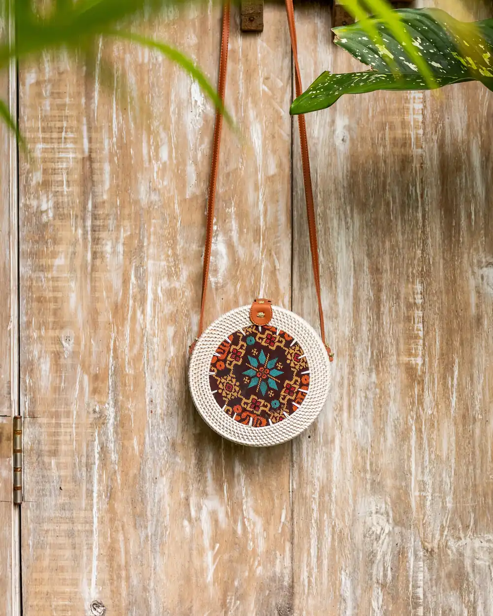 Round Bali rattan bag hanging on a weathered wooden wall